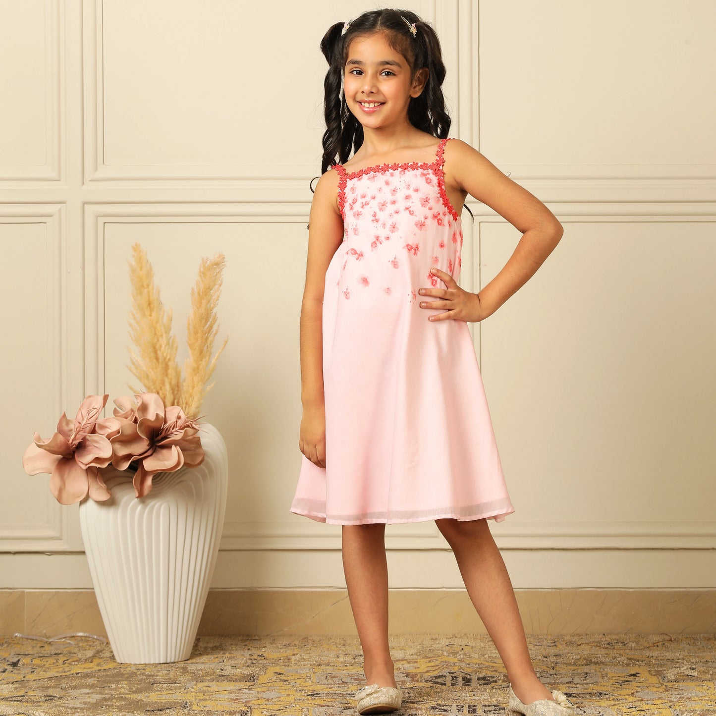 The Eira A-Line Dress is a playful ode to summer blooms. Crafted in a soft pink base, this sleeveless A-line dress features vibrant coral floral embroidery cascading from the neckline, with delicate flower appliqués adding texture and charm.
