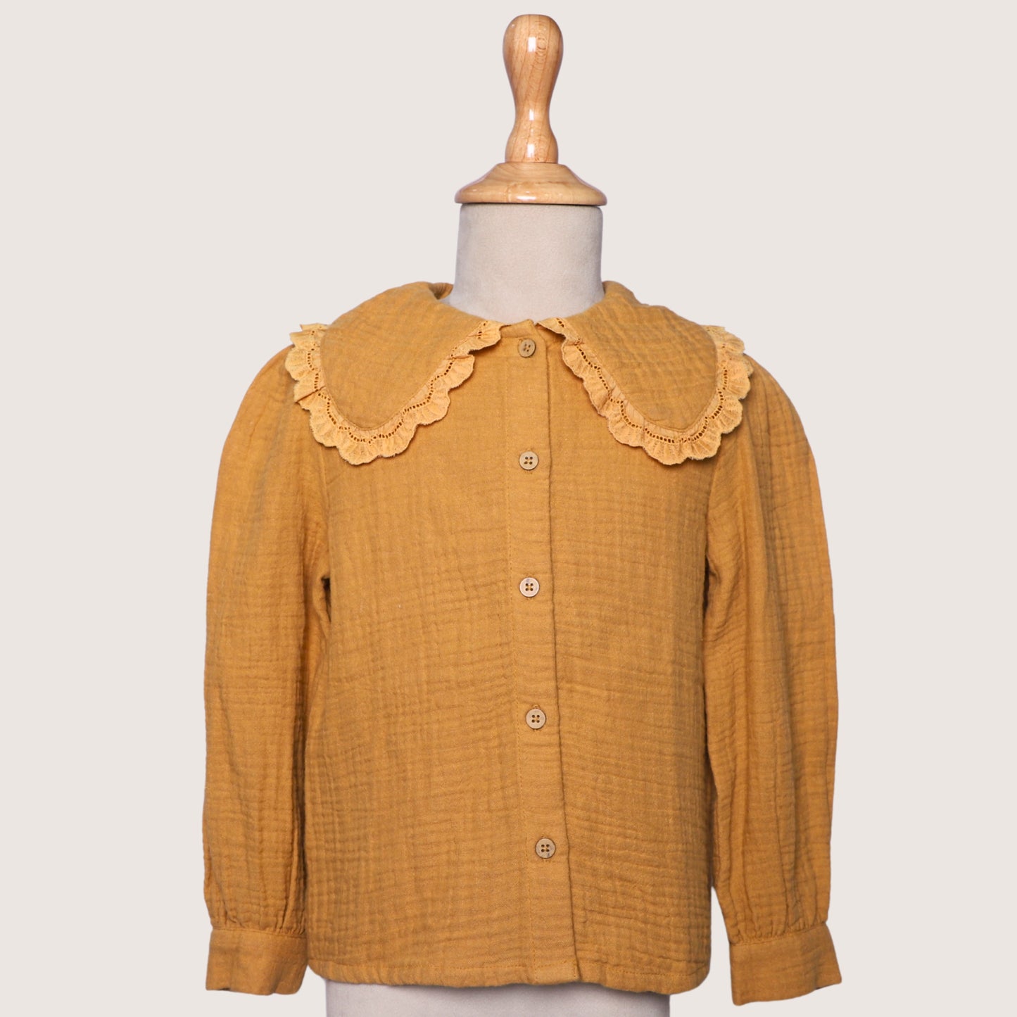 Mustard yellow blouse with lace collar on a mannequin against a white background
