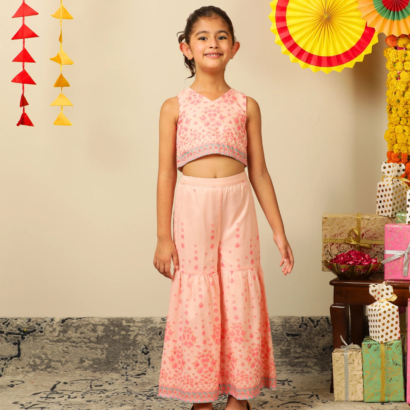 The Meher Sharara Set is a fresh and festive outfit designed for twirls and celebrations. Featuring a sleeveless crop top with a V-neckline and delicate floral embroidery, it’s paired with matching tiered sharara pants