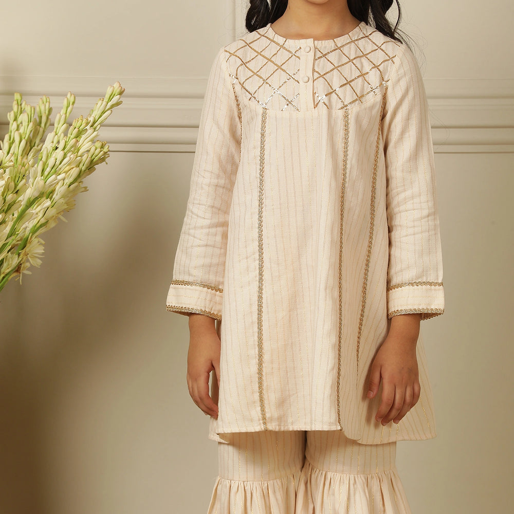 
                  
                    Elegant in its simplicity, the Rajni Sharara Set is a refined ensemble for special occasions. Crafted in a soft ivory-peach hue with subtle&nbsp;pinstripes, this set features a straight-cut kurta with delicate gold threadwork detailing on the yoke and sleeves. 
                  
                