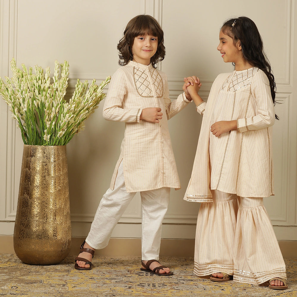 
                  
                    Elegant in its simplicity, the Rajni Sharara Set is a refined ensemble for special occasions. Crafted in a soft ivory-peach hue with subtle&nbsp;pinstripes, this set features a straight-cut kurta with delicate gold threadwork detailing on the yoke and sleeves. 
                  
                