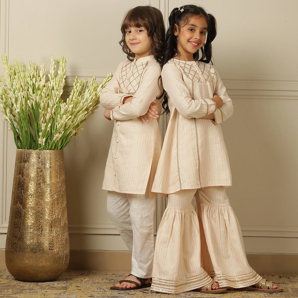 
                  
                    Elegant in its simplicity, the Rajni Sharara Set is a refined ensemble for special occasions. Crafted in a soft ivory-peach hue with subtle&nbsp;pinstripes, this set features a straight-cut kurta with delicate gold threadwork detailing on the yoke and sleeves. 
                  
                