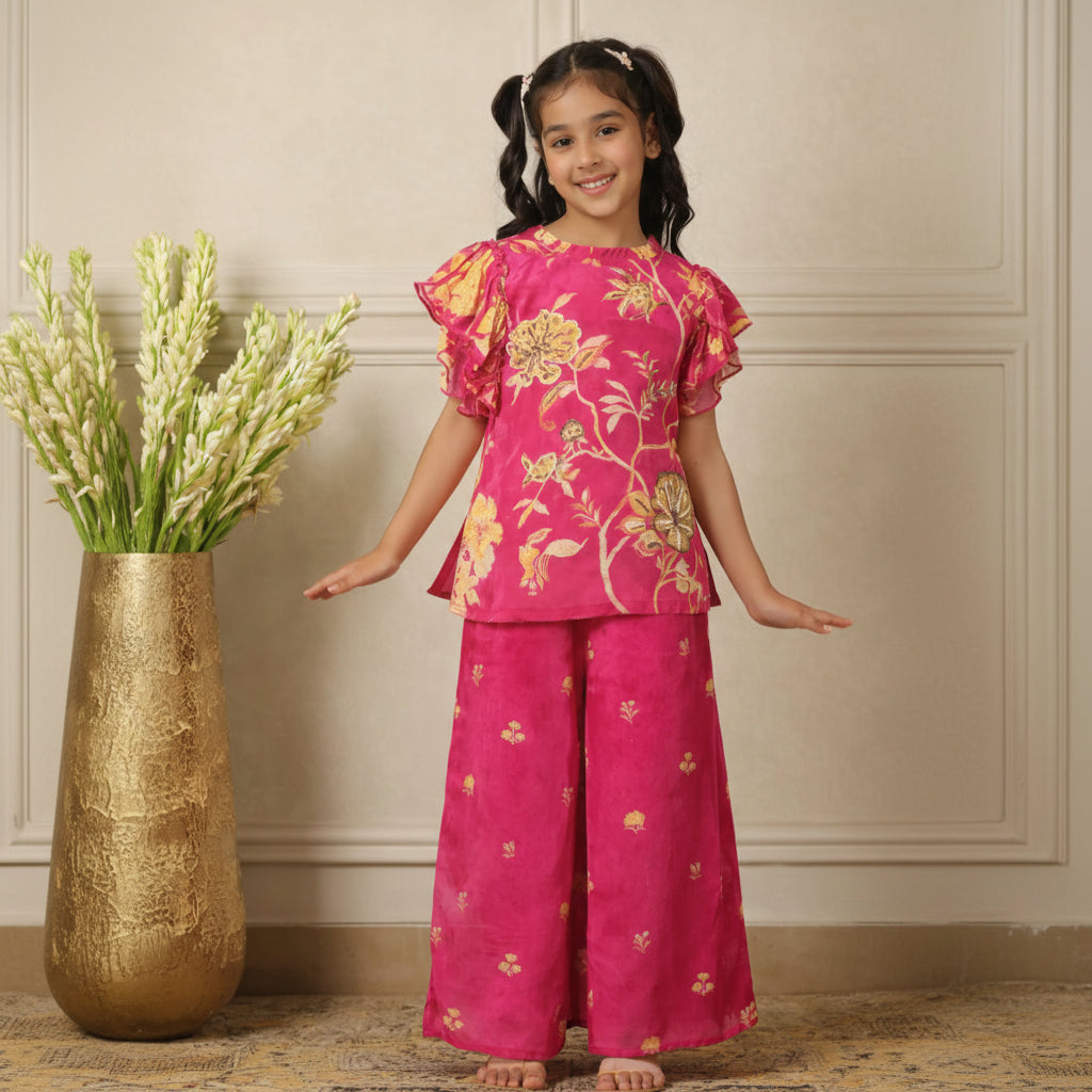 Young girl wearing a pink floral outfit standing against a neutral wall.